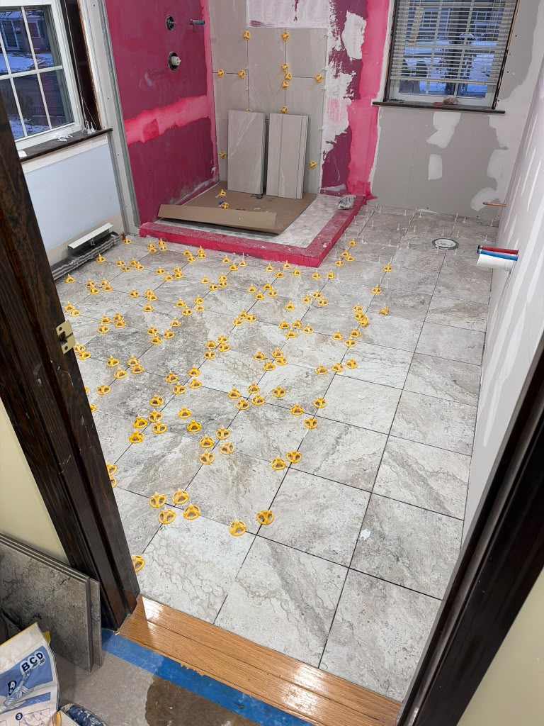 Bathroom floor tile installation with leveling system during a Ronie Construction remodel in Massachusetts